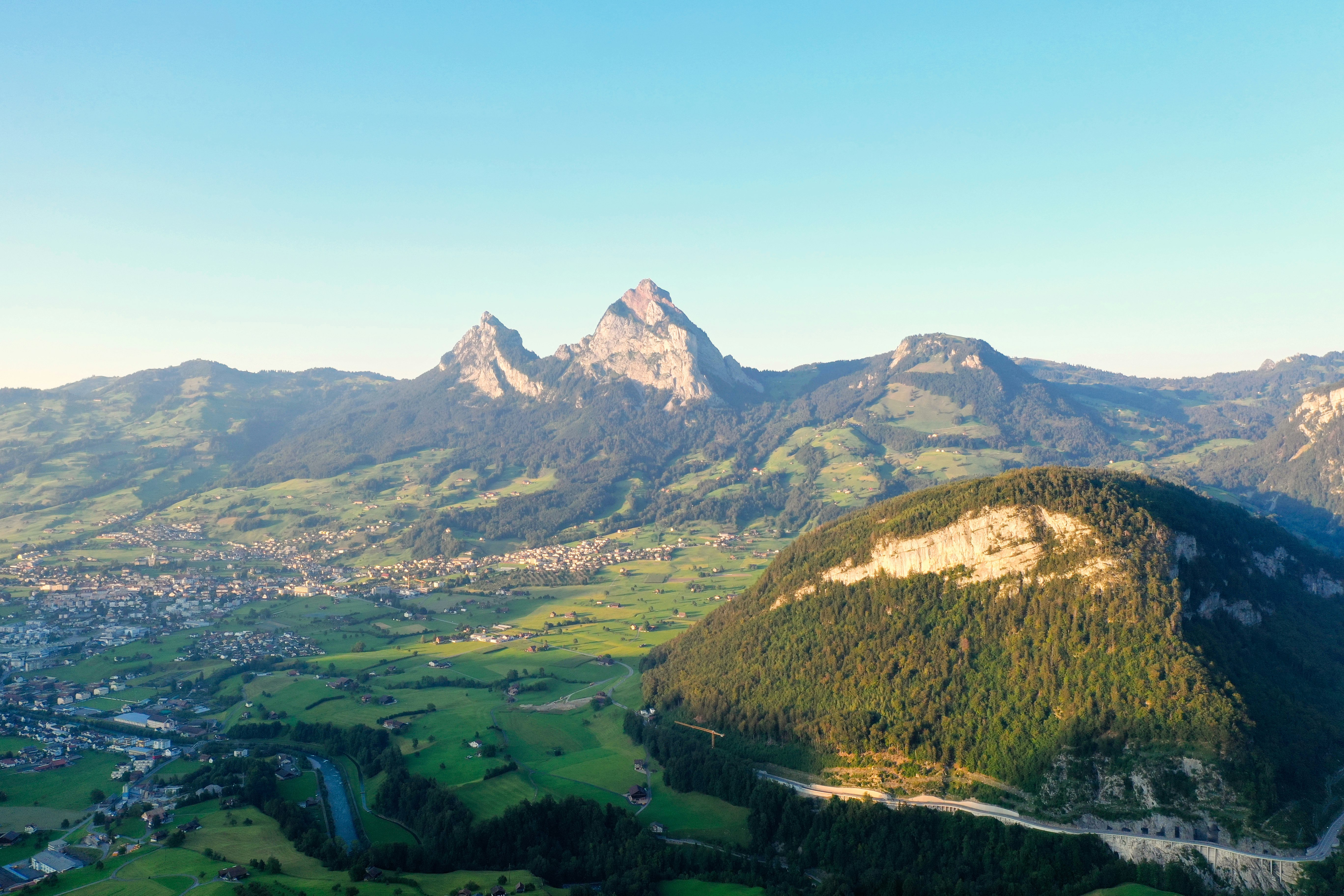 green grass field near mountain under blue sky during daytime